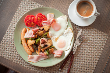 Fried eggs with bacon, sausages, vegetables and a cup of coffee