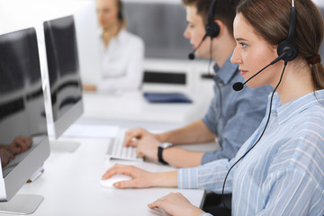 Call center. Group of casual dressed operators at work. Focus on business woman in headset at customer service office. Telesales in business