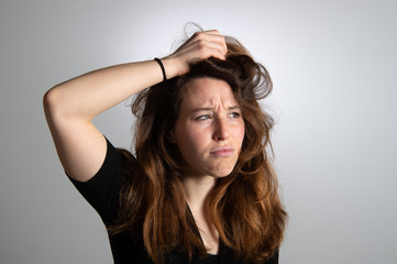 Fototapeta premium Portrait of frustrated young girl holding her long brown hair. Disappointed expression in female face. Isolated on grey background. Emotions...