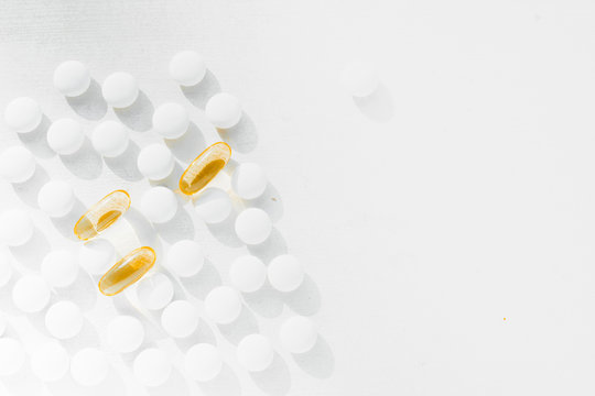 a lot of white round tablets and a few yellow capsules lying on a white background. the view from the top