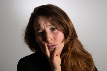 Portrait of sad brunette girl looking at camera over white background. Frowning young woman leaning face on her hand. Emotions in female face...