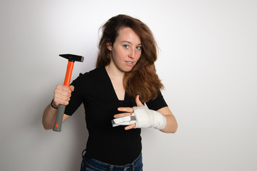 Cheerful brunette woman in black top with white wrist bandage and metal fixation of broken finger. Showing how accident with hammer happened. Pain, accidents and health care concept...