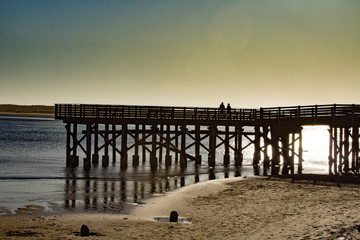 Fototapeta premium Couple Silhouetted on a Wooden Pier at the Beach during sunset