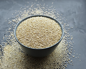 Bowl of healthy white uncooked quinoa seeds on dark stony background