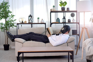Pandemic coronavirus quarantine period concept. National quarantine concept. A man in a gas mask lies on a sofa and reads a book. Stay at home idea. - obrazy, fototapety, plakaty
