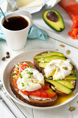 Morning breakfast. Poached egg boiled sandwich with avocado, salmon and coffee on a wooden table.