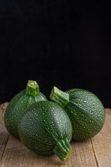 Close-up of three round zucchini on rustic wooden board, selective focus and vertical black background