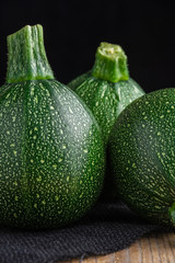 Macro closeup of three round zucchini on rustic wooden board, black burlap rag, selective focus and vertical black background