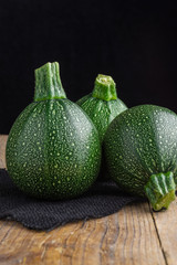 Close-up of three round zucchini on rustic wooden table, black burlap rag, selective focus and vertical black background