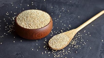 Uncooked quinoa grains in wooden bowl and spoon on black stone background