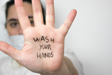 Woman on a side wearing a safety mask with hand opened with the sentence "wash your hands" written on the palm of her hand on a white background. Coronavirus concept.