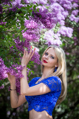 Beautiful blonde near a lilac in a blue top. Vertical orientation