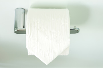White toilet roll on a silver toilet-roll holder, with a plain background, landscape orientation 