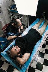 A high angle shot of a tattoo artist creating a tattoo on a man's arm under a softbox lighting