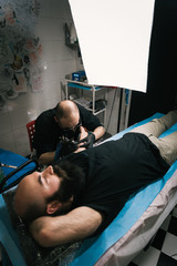A high angle shot of a tattoo artist creating a tattoo on a man's arm under a softbox lighting