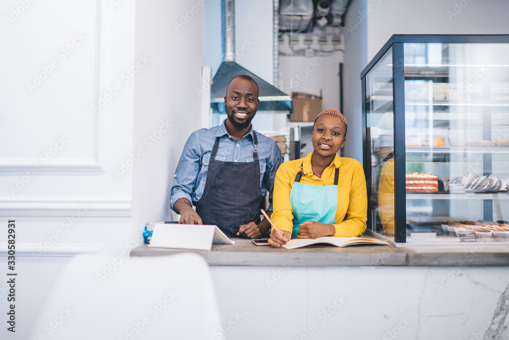 Wall mural Young couple of pastry shop owners standing at counter