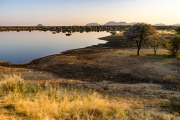 Namibia, Africa. Southeast of Omaruru. Winter sunrise over a waterhole with wild birds and reflections.