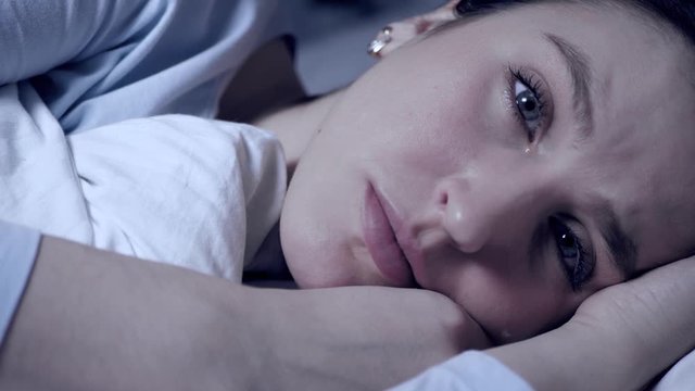 Girl is crying at night. Resentment, frustration, problems in personal life, problems in relationships concept. Attractive woman lies in bed looking at camera and tears flow down her face. Close-up