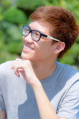 Asian handsome teenage boy wearing glasses fun, Portrait cheerful hipster young man are smiling and laugh with a happy face at park on green nature background in Thailand