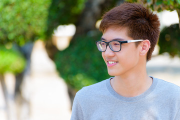 Asian handsome teenage boy wearing glasses, Portrait cheerful hipster young man are smile with a happy face at park on green nature background in Thailand