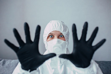 a virologist in a white protective suit with a black mask and medical gloves with fear on face shows hands into the camera. Doctor struggling with an epidemic coronavirus