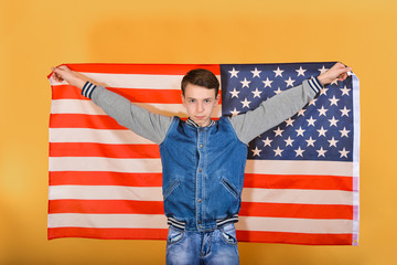 A teenager boy holds an American flag in his hands behind his back.
