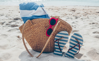 Straw bag, sunglasses and flip flops on a tropical sand beach. Travel, vacation concept.