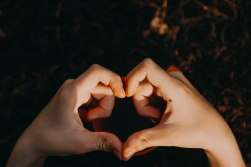 A mug of tea standing on the grass. The heart of the fingers above the Cup. Love.