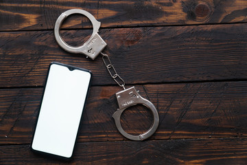 smartphone with blank screen for your text or logo with handcuffs rests on a wooden background