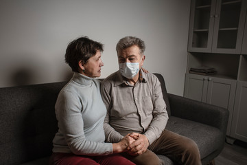 A couple sitting on a sofa wearing a protective mask. An infectious agent protection gear  including a mask. An sick older man and woman wearing protective masks to protect against virus. Coronavirus.