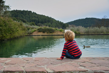 Blond boy watching the water raft with ducks