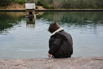 Dark boy watching the water raft with ducks,