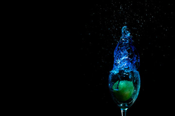 Lemon fell into a glass with blue water, a beautiful splash, cocktail on a black background