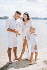 Young family with kids in white clothes walking on the sandy beach, they have fun.