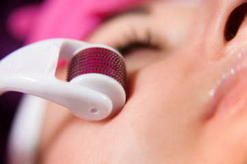 Doctor cosmetologist makes facial massage procedure using a dermo roller. Woman in beauty salon...