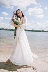 Fototapeta na wymiar beautiful girl in a white dress and holds a bouquet of flowers on the beach