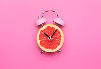 Creative alarm clock made of citrus fruit on color background