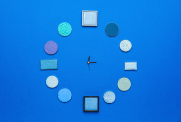 Creative clock made of eyeshadows on color background
