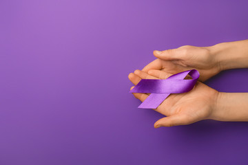 Female hands with violet ribbon on color background. Domestic violence concept