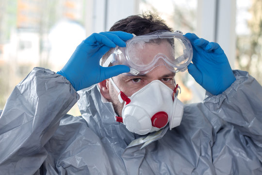 Zmęczony , spocony mężczyzna ubrany w kombinezon ochronny i maskę ochronną na twarz zdejmuje gogle ochronne i rozbiera się po skończonej pracy.
