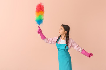 Little housewife with dust brush on color background