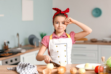 Crying little housewife cutting fresh onion in kitchen