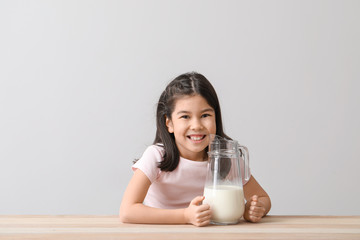 Cute Asian girl with milk on light background