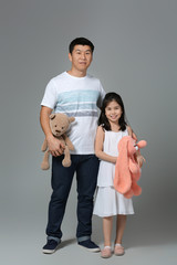 Happy Asian man and his little daughter with toys on grey background