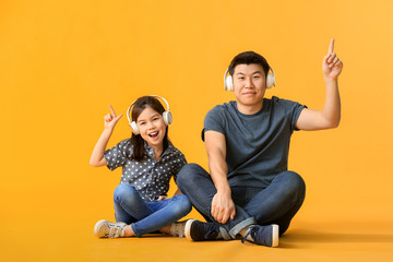 Happy Asian man and his little daughter listening to music on color background