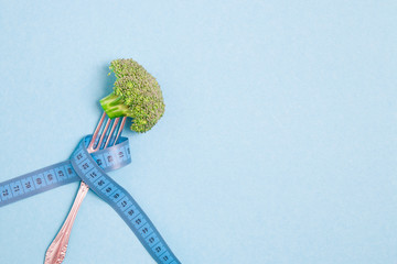one broccoli on a fork wrapped in blue measuring tape on a blue background place copy top view diet...