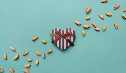 Heart shaped gift box among scattered almond with copy space to the left. View from above.