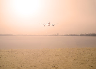 Fototapeta na wymiar Airplane over the lake in the orange sky with the sun. Nature and transport
