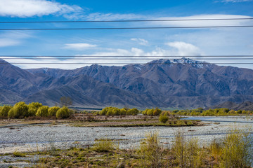 Beautiful dry river with leafy trees on the sides and snow capped mountains in the background taken on a sunny day, New Zealand