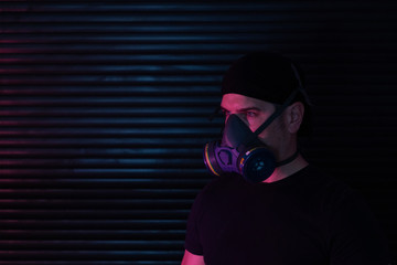 A man wearing a breathing mask, dressed in black looking left against dark background and reddish lighting